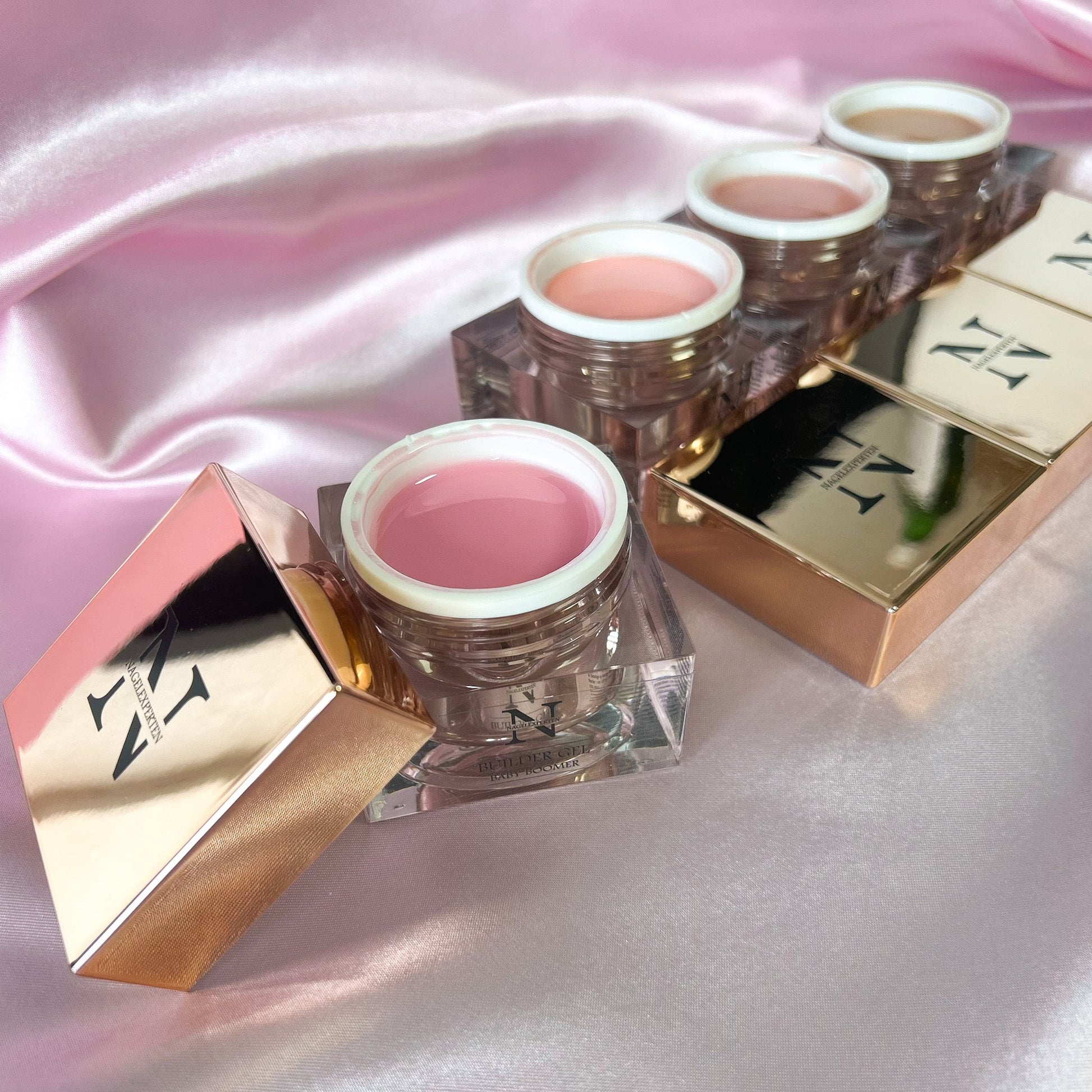 Fyra builder gels som ligger på en rosa sidenduk i färgerna ljusrosa, beige och nude.
