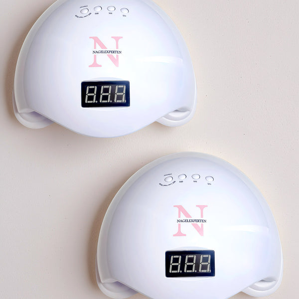 Två vita nagellampor från Nagelexperten för härdning av nagelprodukter som står på ett vitt bord.