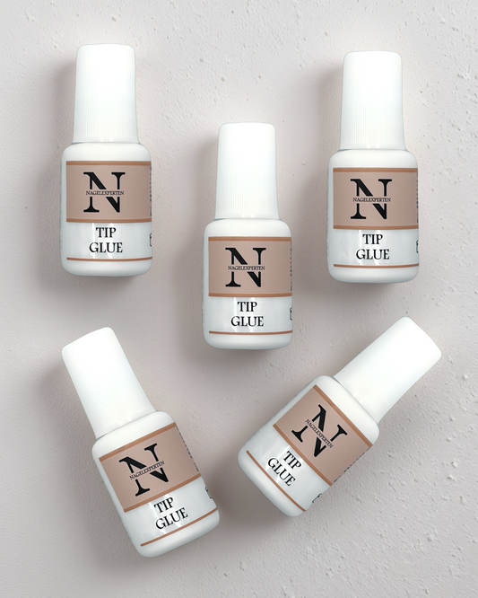 5 stycken nagellim med pensel liggandes på ett beige bord.